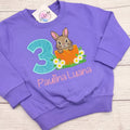 Hase Geburtstagsshirt Mädchen personalisiert – lila Sweatshirt mit Hasen im Ei, türkiser Glitzerzahl und Name